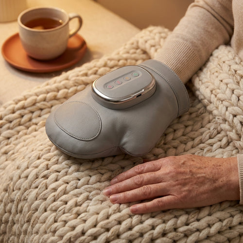 Hand resting inside the gray heated hand massager on a knit blanket